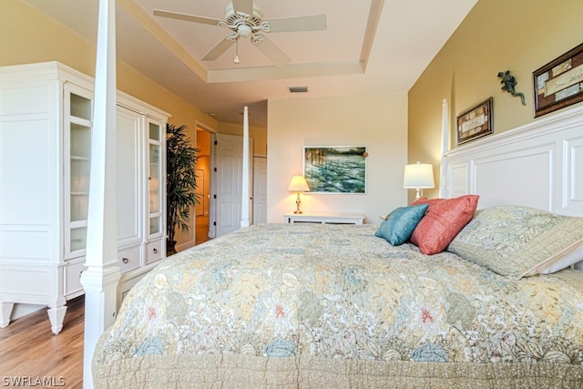 bedroom featuring ceiling fan, light wood-type flooring, and a tray ceiling