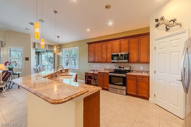 kitchen featuring tasteful backsplash, stainless steel appliances, pendant lighting, sink, and light stone countertops