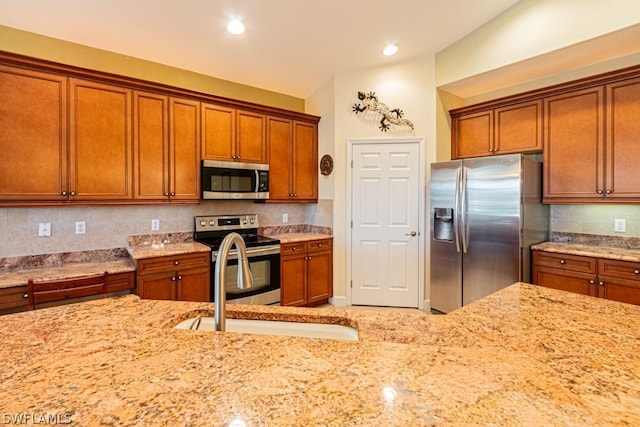 kitchen featuring decorative backsplash, stainless steel appliances, light stone counters, and sink