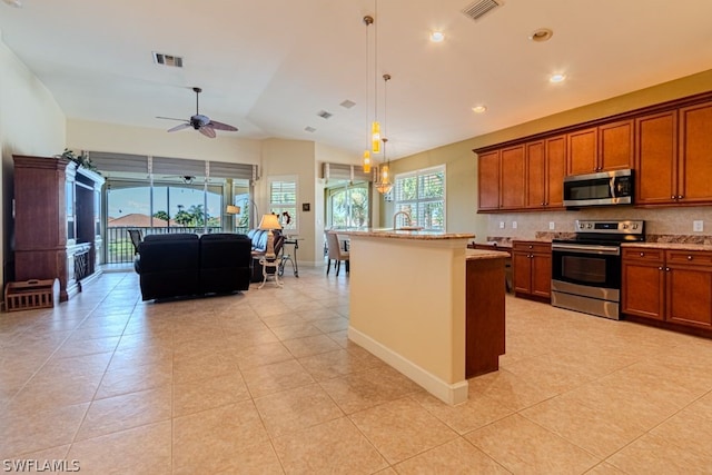 kitchen featuring decorative light fixtures, ceiling fan, tasteful backsplash, stainless steel appliances, and an island with sink