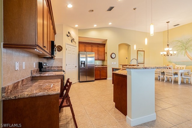 kitchen featuring appliances with stainless steel finishes, tasteful backsplash, decorative light fixtures, light tile patterned floors, and an island with sink