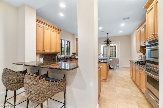 kitchen featuring dark stone countertops, a kitchen breakfast bar, decorative backsplash, hanging light fixtures, and kitchen peninsula