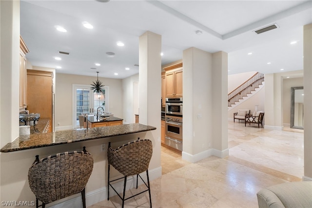 kitchen with sink, dark stone countertops, hanging light fixtures, kitchen peninsula, and stainless steel double oven