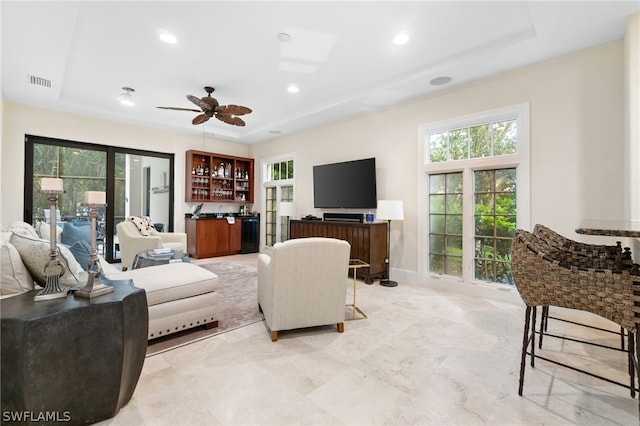 living room with bar area, ceiling fan, and a tray ceiling