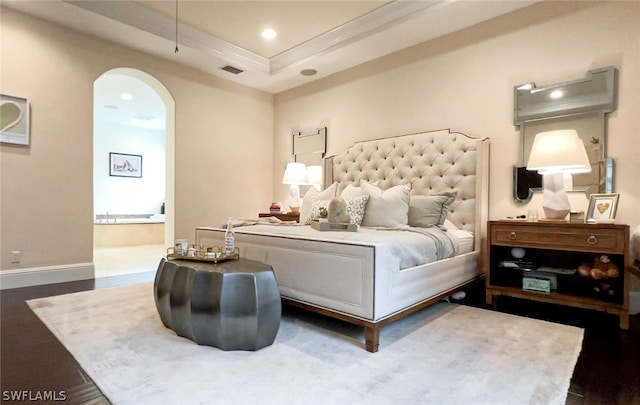 bedroom with hardwood / wood-style floors, ornamental molding, connected bathroom, and a tray ceiling