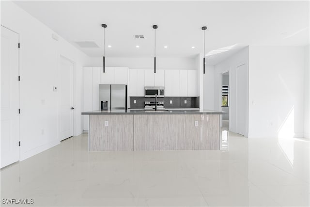 kitchen with a kitchen island with sink, white cabinets, stainless steel appliances, and decorative light fixtures