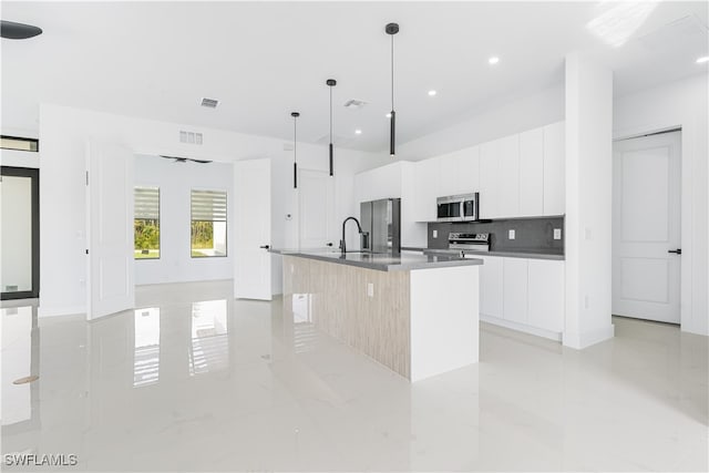 kitchen with stainless steel appliances, ceiling fan, pendant lighting, white cabinetry, and an island with sink