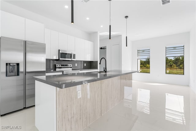 kitchen featuring stainless steel appliances, a kitchen island with sink, sink, decorative light fixtures, and white cabinets