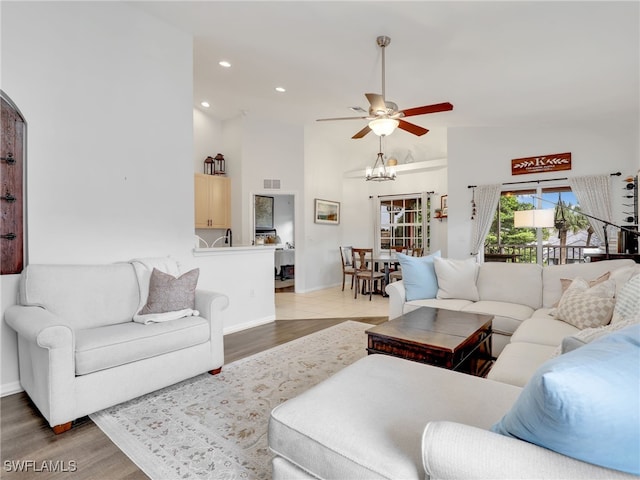 living room with ceiling fan with notable chandelier, wood-type flooring, and a towering ceiling