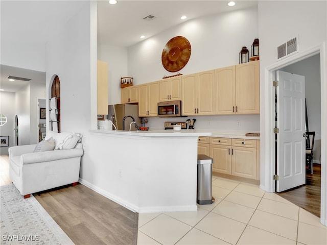 kitchen with kitchen peninsula, light brown cabinets, light wood-type flooring, and a high ceiling