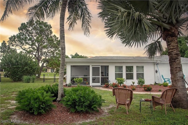 back house at dusk featuring a sunroom and a yard