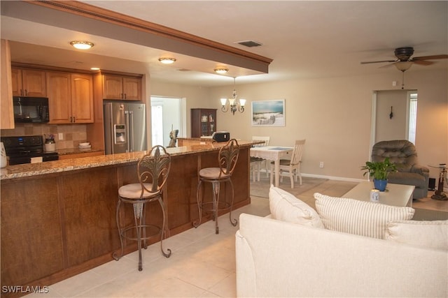 kitchen featuring pendant lighting, backsplash, black appliances, a kitchen breakfast bar, and light stone counters