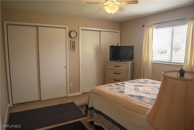 bedroom with ceiling fan, light colored carpet, and two closets