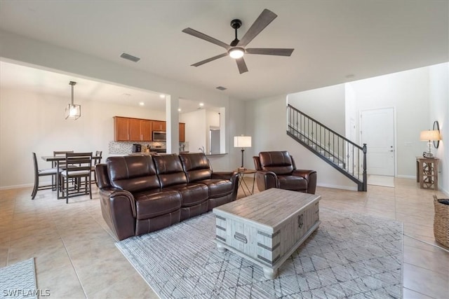 living area with ceiling fan, light tile patterned floors, visible vents, baseboards, and stairs