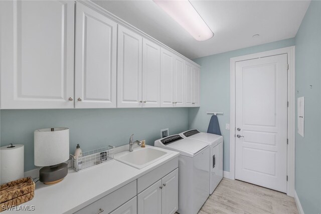 laundry area with sink, cabinets, washer and clothes dryer, and light hardwood / wood-style flooring