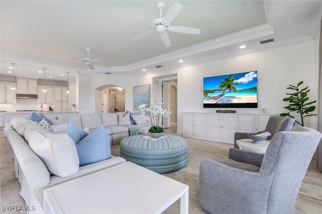 living room with a raised ceiling, crown molding, light wood-type flooring, and ceiling fan