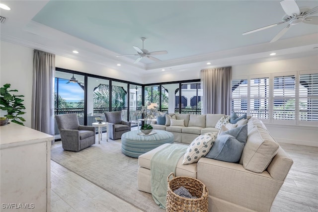 living room featuring a raised ceiling, light wood-type flooring, and ceiling fan