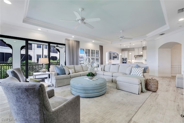 living room featuring ceiling fan, a raised ceiling, and ornamental molding