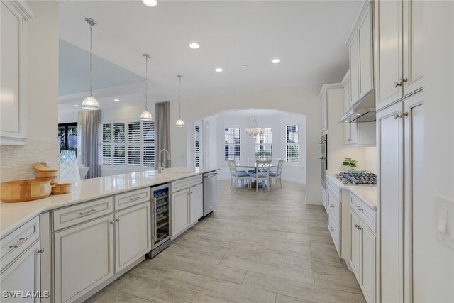 kitchen featuring appliances with stainless steel finishes, hanging light fixtures, decorative backsplash, beverage cooler, and wall chimney exhaust hood