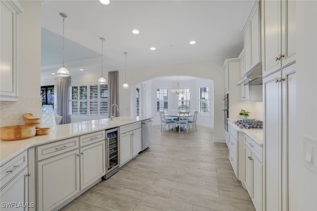 kitchen with white cabinetry, pendant lighting, stainless steel appliances, beverage cooler, and backsplash