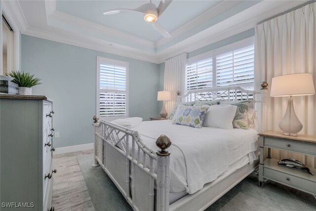 bedroom with light hardwood / wood-style floors, a raised ceiling, crown molding, and ceiling fan