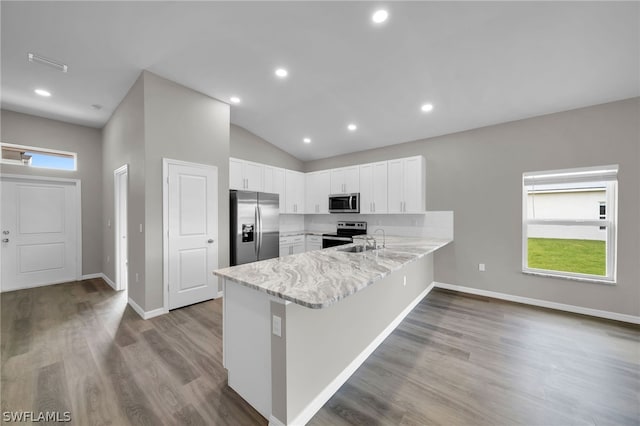 kitchen featuring appliances with stainless steel finishes, white cabinets, hardwood / wood-style floors, kitchen peninsula, and lofted ceiling