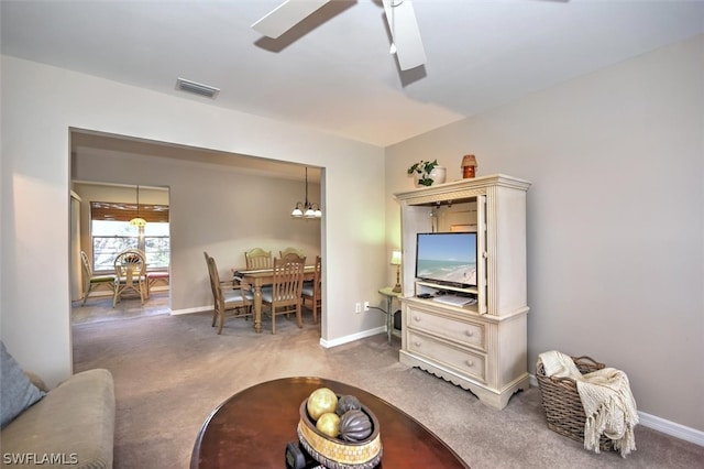 carpeted living room with ceiling fan with notable chandelier