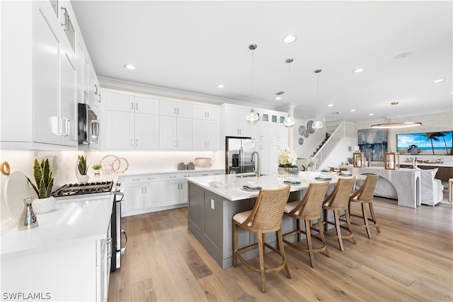 kitchen with appliances with stainless steel finishes, a breakfast bar, a center island with sink, white cabinetry, and hanging light fixtures