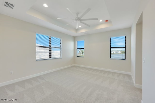 carpeted spare room with ceiling fan, plenty of natural light, and a raised ceiling