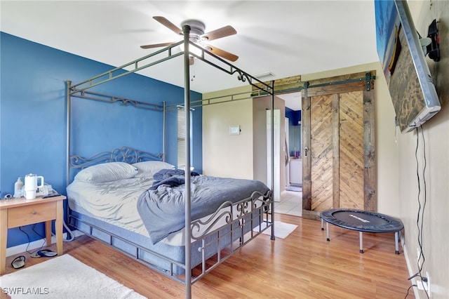 bedroom featuring light hardwood / wood-style floors, ceiling fan, and a barn door