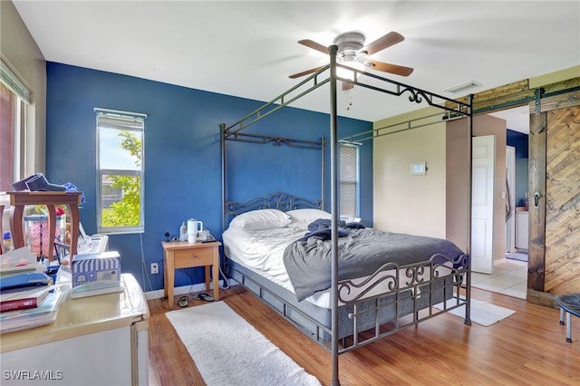 bedroom with ceiling fan, light hardwood / wood-style flooring, and a barn door