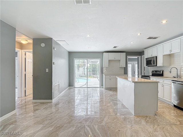 kitchen featuring white cabinets, appliances with stainless steel finishes, backsplash, and a center island