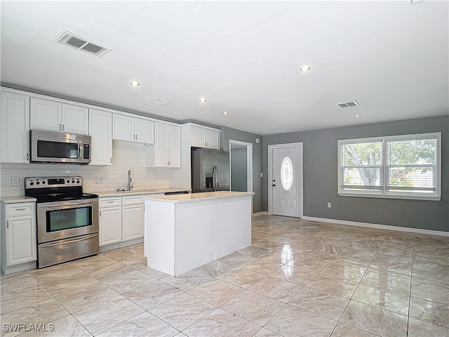 kitchen featuring a center island, sink, white cabinets, decorative backsplash, and appliances with stainless steel finishes