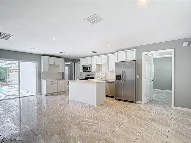 kitchen with appliances with stainless steel finishes, decorative backsplash, white cabinetry, a kitchen island, and sink