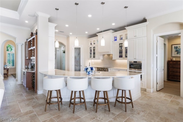 kitchen with stainless steel oven, backsplash, a kitchen breakfast bar, decorative light fixtures, and white cabinetry