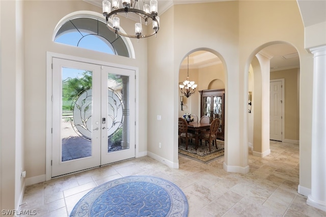 foyer featuring french doors, a towering ceiling, an inviting chandelier, and crown molding