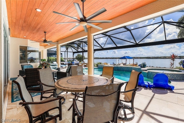 view of patio with a lanai, ceiling fan, a swimming pool with hot tub, and a water view