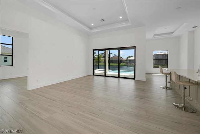 unfurnished living room featuring a tray ceiling, light hardwood / wood-style flooring, and a wealth of natural light