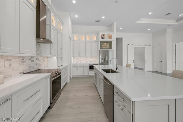 kitchen featuring a spacious island, sink, stainless steel appliances, a barn door, and wall chimney range hood