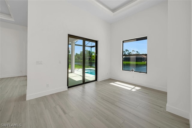 unfurnished room featuring a tray ceiling, light hardwood / wood-style flooring, and a water view