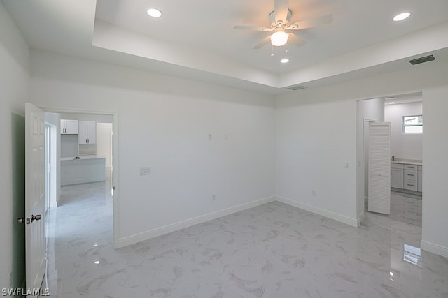 spare room with a tray ceiling, ceiling fan, and light tile patterned floors