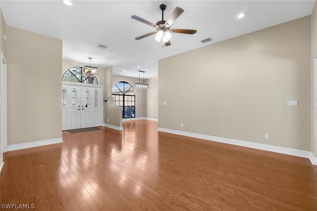 unfurnished living room featuring ceiling fan with notable chandelier and hardwood / wood-style floors