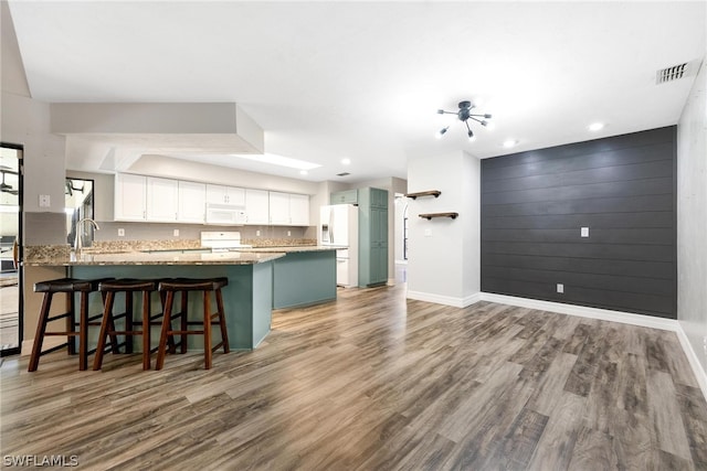 kitchen with light stone countertops, hardwood / wood-style flooring, white cabinets, and white appliances