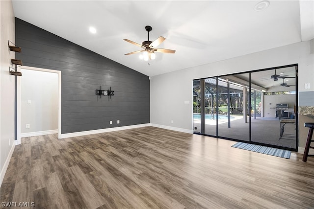 empty room featuring wooden walls, ceiling fan, wood-type flooring, and vaulted ceiling