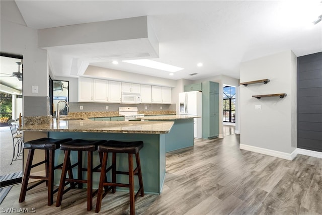 kitchen with white cabinetry, white appliances, sink, light hardwood / wood-style floors, and kitchen peninsula