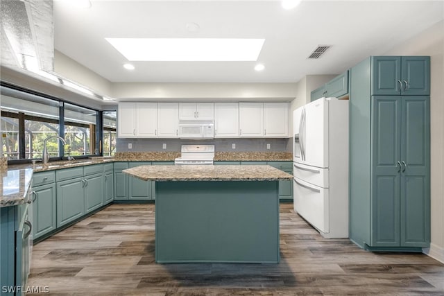 kitchen with white appliances, hardwood / wood-style floors, sink, a skylight, and a center island