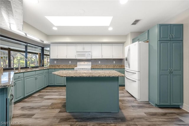 kitchen with sink, white appliances, a skylight, a center island, and white cabinets