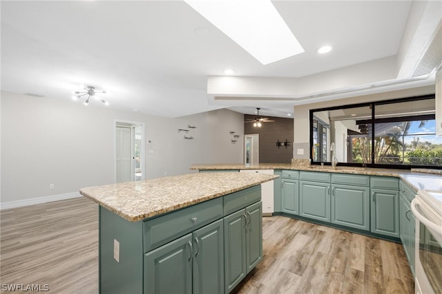 kitchen featuring light hardwood / wood-style flooring, green cabinetry, a kitchen island, a skylight, and ceiling fan