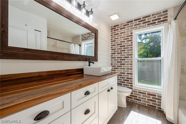 full bathroom with brick wall, vanity, toilet, and plenty of natural light