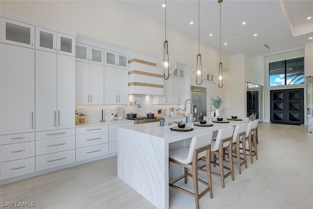 kitchen with hanging light fixtures, appliances with stainless steel finishes, an island with sink, white cabinets, and a high ceiling